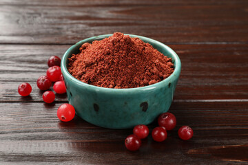 Dried cranberry powder in bowl and fresh berries on wooden table