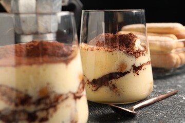 Delicious tiramisu in glasses and spoon on grey textured table, closeup