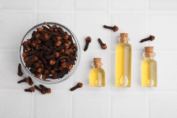 Clove oil in bottles and bowl with dried buds on white tiled table, flat lay
