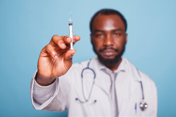 Close-up of doctor wearing white lab coat holding a syringe with hypodermic needle filled with...