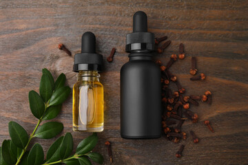 Clove oil in bottles, leaves and dried buds on wooden table, flat lay
