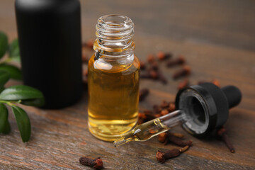 Clove oil in bottle, pipette, leaves and dried buds on wooden table, closeup