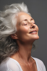 A gorgeous happy smiling senior woman with closed eyes and long grey hair over a grey background