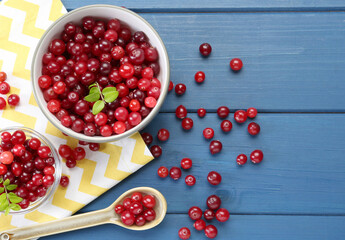 Fresh ripe cranberries in bowls and spoon on blue wooden table, flat lay