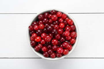 Fresh ripe cranberries in bowl on white wooden table, top view