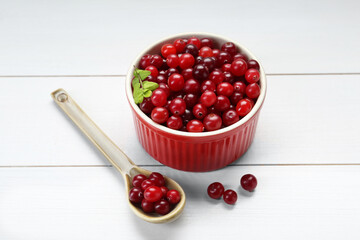 Fresh ripe cranberries in bowl and spoon on white wooden table, closeup