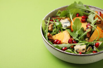Tasty salad with persimmon, blue cheese, pomegranate and walnuts served on light green background, closeup. Space for text
