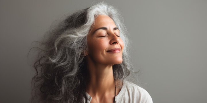 A Gorgeous Happy Smiling Senior Woman With Closed Eyes And Long Grey Hair Over A Grey Background