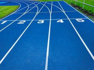 Blue running track with starting line numbers one to five. Isolated on blue background for sports and athletics concept. Empty track for copy space and text overlay. Top view of running track.