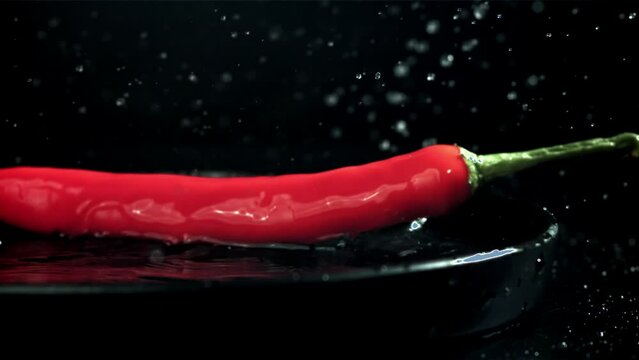 The chili peppers fall with splashes into the plate. On a black background. Filmed on a high-speed camera at 1000 fps. High quality FullHD footage