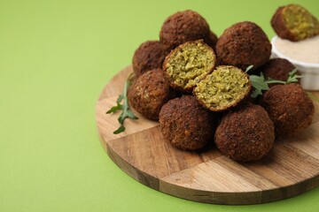 Delicious falafel balls, arugula and sauce on green background, space for text