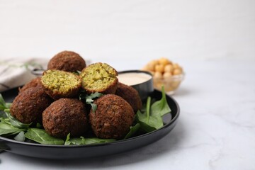 Delicious falafel balls, herbs and sauce on white marble table, closeup