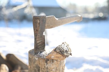 Metal axe in wooden log on sunny winter day, closeup