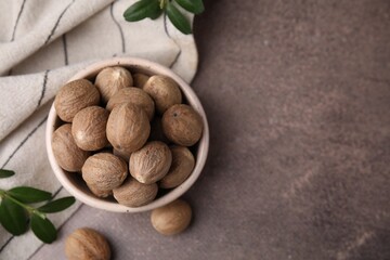 Whole nutmegs in bowl and green branches on brown table, flat lay. Space for text
