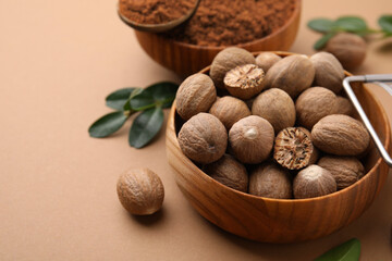 Nutmeg powder and seeds on light brown background, closeup. Space for text