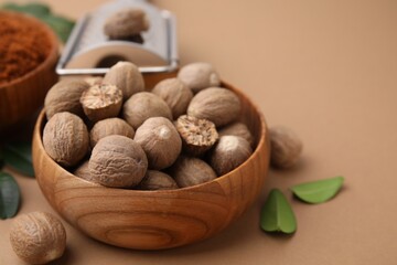 Nutmegs in bowl on light brown background, closeup. Space for text