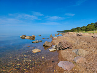 Serene and Picturesque Rocky Beach with Large Stones and Boulders, Glistening in the Sunlight on a Beautifully Clear Day, with a Vibrant Blue Sky and Wispy Clouds Adding a Touch of Drama to the Scene
