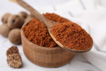 Bowl and spoon with nutmeg powder on white table, closeup