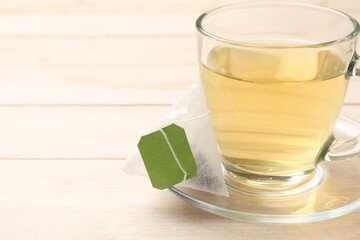 Tea bag and glass cup on light wooden table, closeup. Space for text