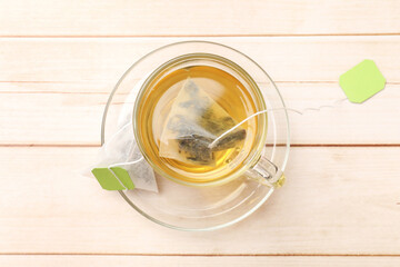 Tea bag in glass cup on light wooden table, top view