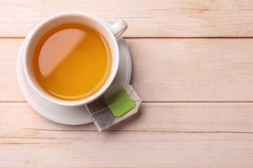 Tea bag and cup of hot beverage on light wooden table, top view. Space for text