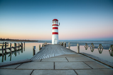Lighthouse in red and white colours on a lake dock with a clear sky at sunrise