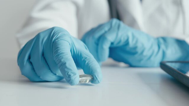 The doctor carefully examines the pharmaceutical capsules, ready to give appropriate recommendations for the patient. In a medical gown, goggles and gloves in hand pill, capsule medication tablet