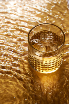 Whiskey glass with ice on a textured golden surface