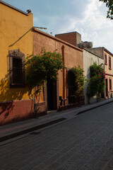 Fototapeta na wymiar Street in the historic center of the city of Queretaro, Mexico. On this street you can see some historic or old houses while the beautiful evening sun is hitting them, outside the houses there are inc