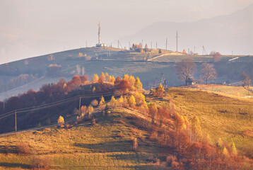 Panoramic view of misty sunny autumn evening in mountains. Beautiful sunset hills landscape. Slopes, meadows, fields, village, house, dirt road. Amazing fall rural scene. Carpathian range.