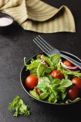 Green salad leaves in bowl on black table.