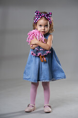 Adorable blonde little girl on gray background, holding a doll