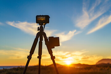 Camera on tripod taking picture of sunset over coast