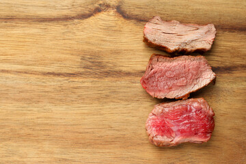 Delicious sliced beef tenderloin with different degrees of doneness on wooden table, top view. Space for text