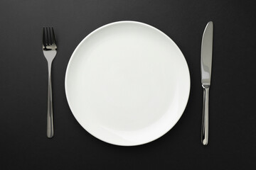 Empty plate, fork and knife on black table, top view