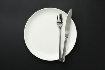 Clean plate, fork and knife on black table, top view