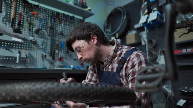 Male bicycle mechanic in repair shop making repair of bike wheel. Replacing rear hub bearings. Reassembly of cycle hub ball bearings and lubricating. Cycle repairman at work. Technician in workshop. 