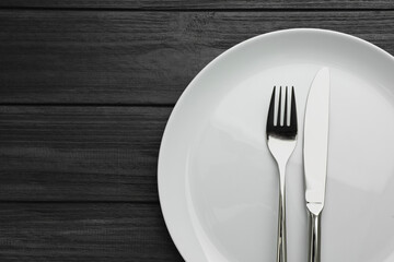 Clean plate and cutlery on black wooden table, top view