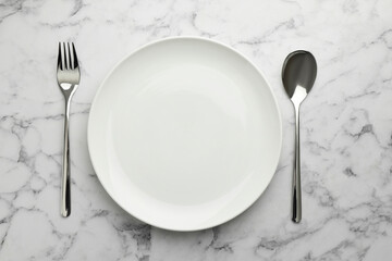 Empty plate, fork and spoon on white marble table, top view