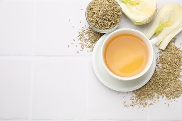 Fennel tea in cup, seeds and fresh vegetable on white tiled table, flat lay. Space for text