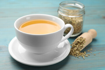 Fennel tea in cup and seeds on light blue wooden table, closeup