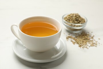 Fennel tea in cup and seeds on white marble table, closeup