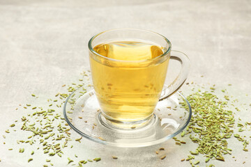 Aromatic fennel tea in cup and seeds on light grey table, closeup