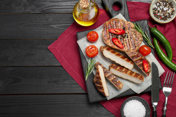 Grilled pork steaks with rosemary, spices, vegetables and cutlery on dark wooden table, top view....