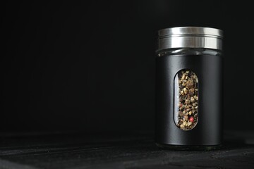 Pepper shaker on wooden board against black background. Space for text