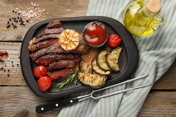 Delicious grilled beef with vegetables, tomato sauce and spices on wooden table, top view
