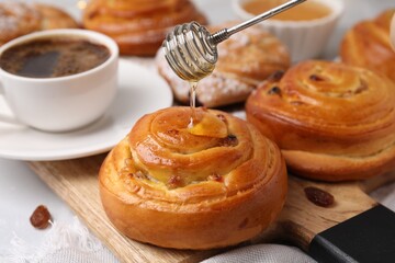 Pouring honey onto delicious rolls with raisins at table, closeup. Sweet buns