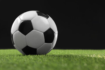Soccer ball on green grass against black background, space for text