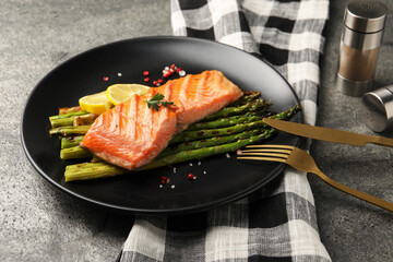 Tasty grilled salmon with asparagus, lemon and spices served on grey table, closeup