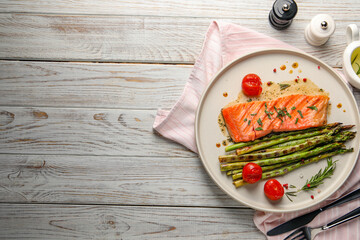 Tasty grilled salmon with tomatoes, asparagus and spices served on wooden table, flat lay. Space...